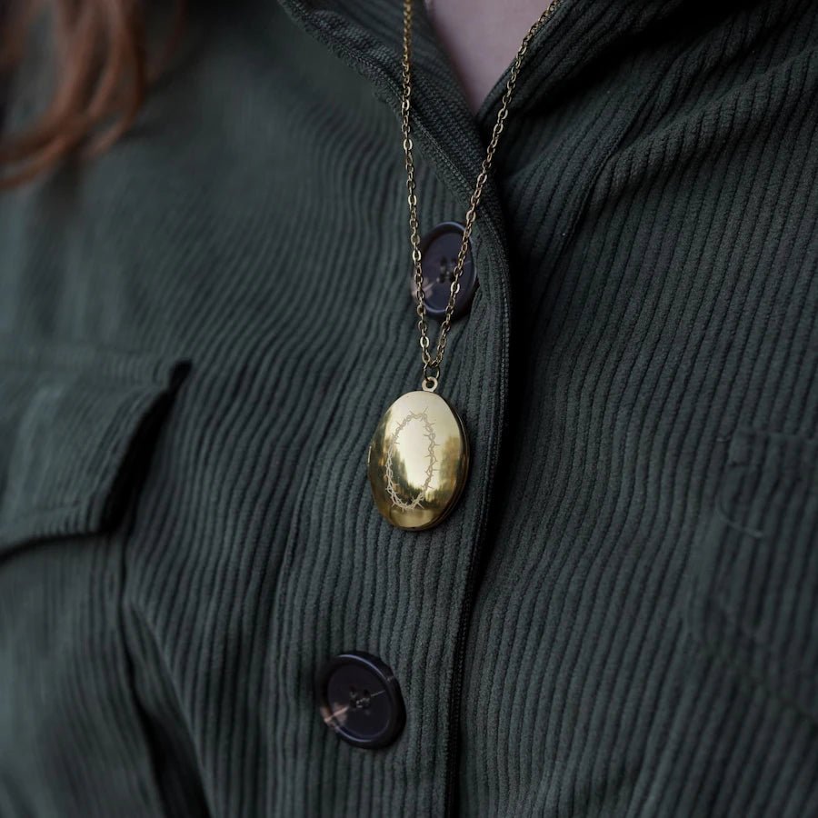 The Dark Artifices Jesse Blackthorn Replica Locket is gold with a wreath of thorns etched on the front and sabers on back.