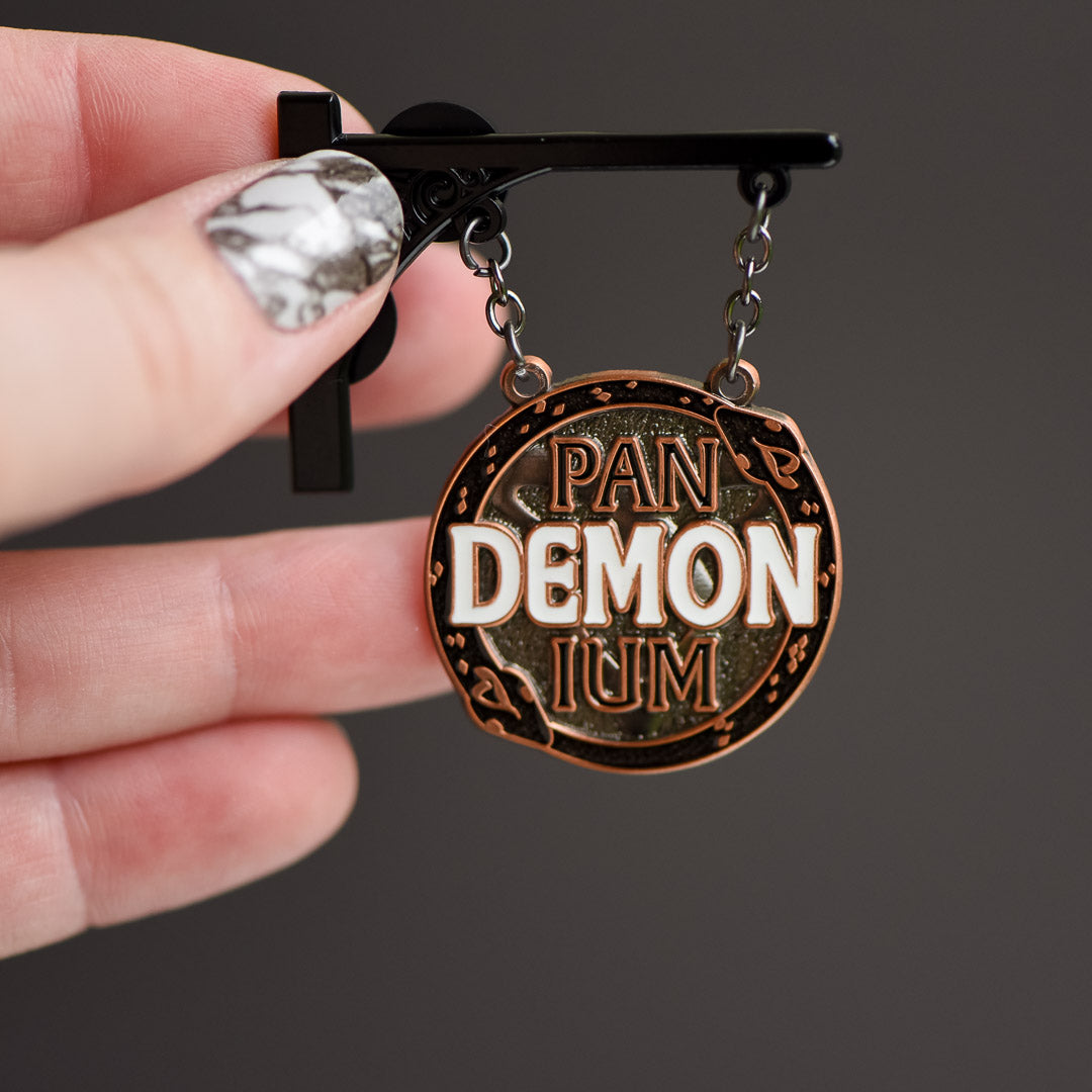 Pandemonium Club Pin is an enamel pin bracket with chains holding a circular hanging sign with &quot;DEMON&quot; in large white letters.