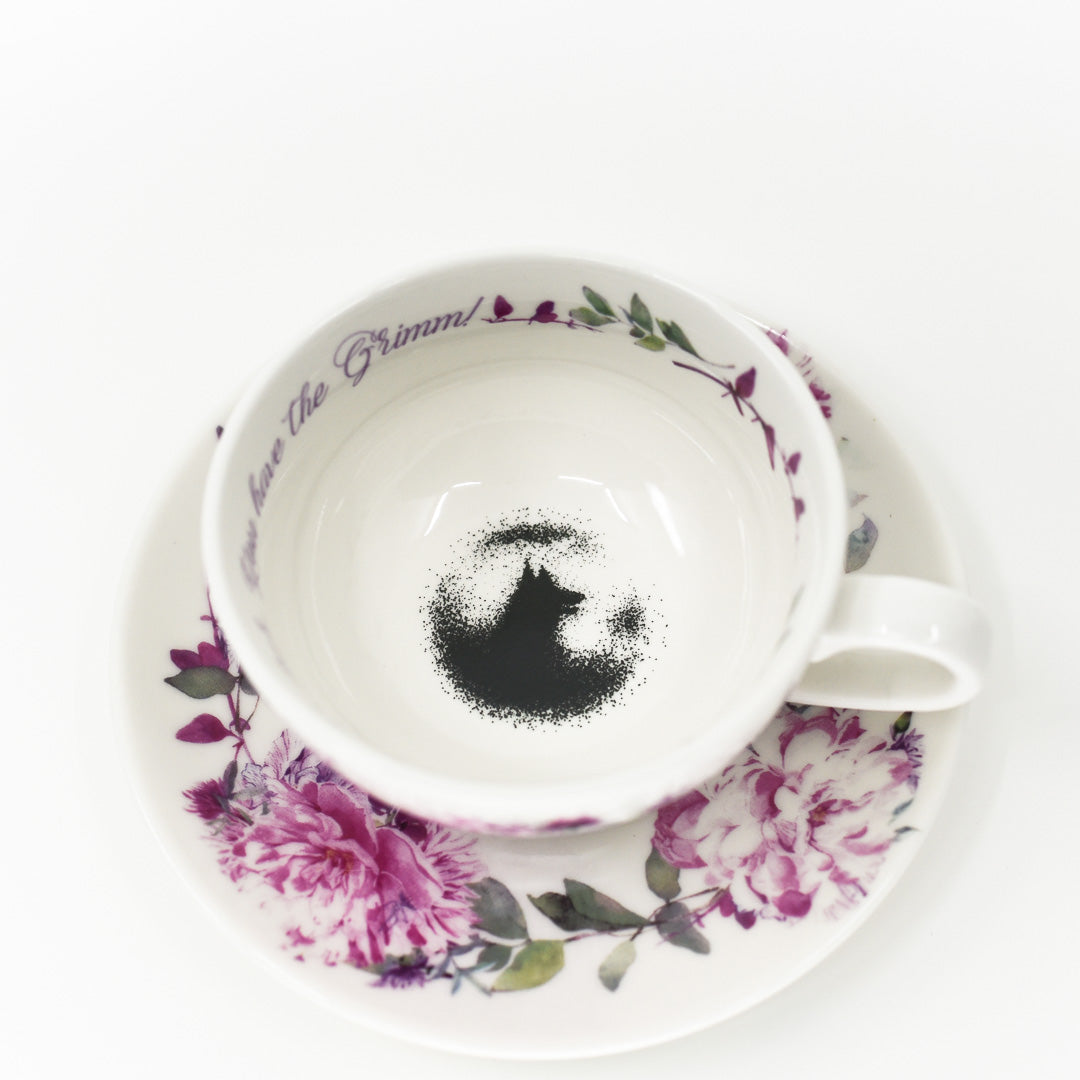 Grimm Teacup and Saucer has a small plate and teacup with violet flowers. A wolf and the words &quot;you have the grimm&quot; are on the inside