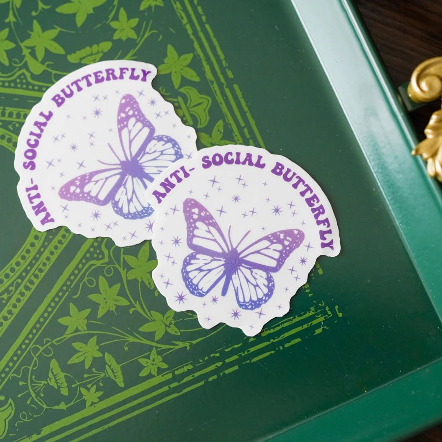 A sticker that reads &quot;Antisocial Butterfly&quot; in purple text above an ombre purple butterfly surrounded by sparkle icons.
