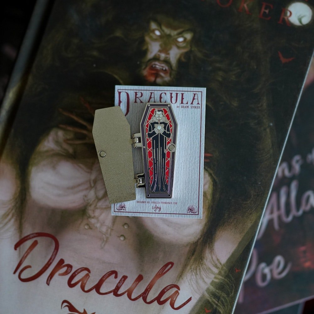 Dracula&#39;s Coffin Hinge Enamel Pin features vampire art with a cross, roses, and bats on the outside and Dracula inside.