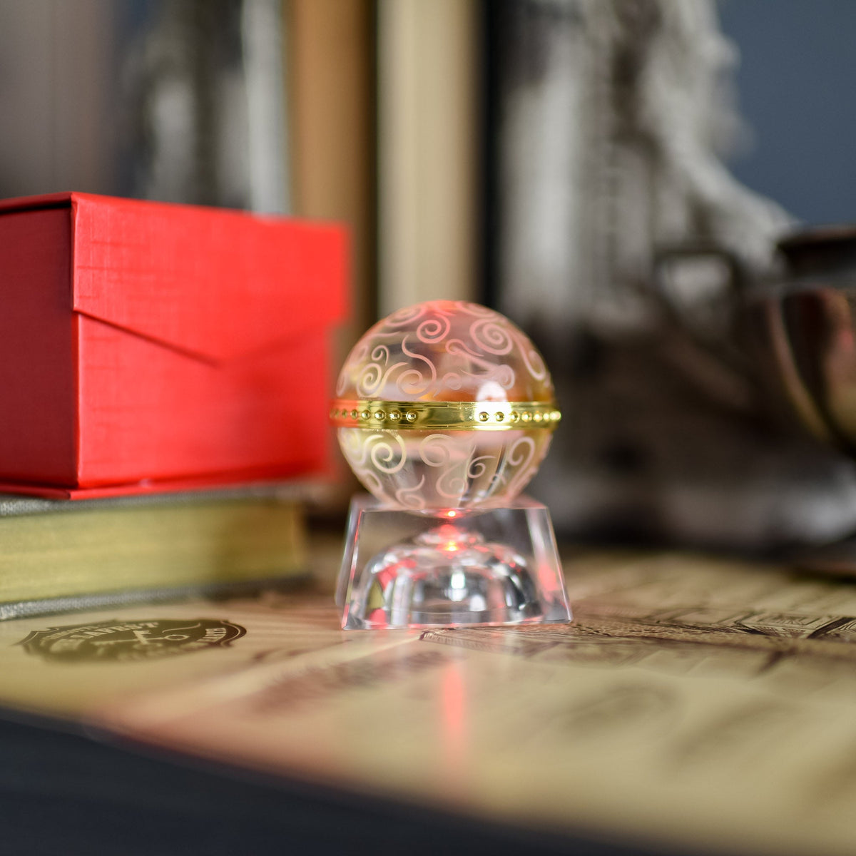 a clear crystal Memory ball with swirled etching and a gold ring around the middle sitting on crystal stand with red light.