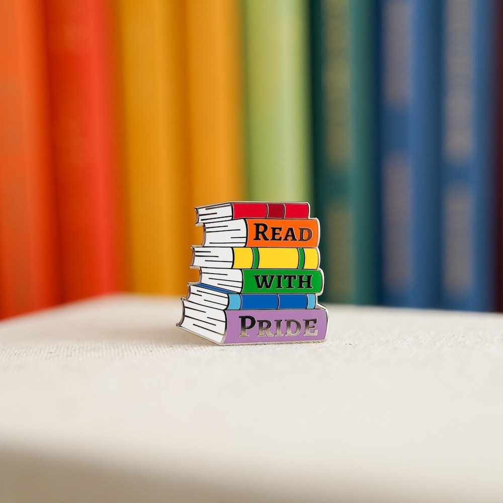 Pride Pin Set with a stack of rainbow colored books that say &quot;Read With Pride&quot;