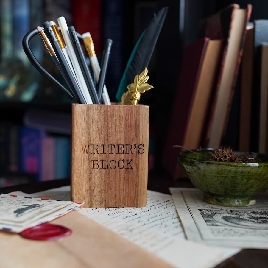 Writer's Block Pen Holder is a wooden pen cup with "writer's block" written on the side.