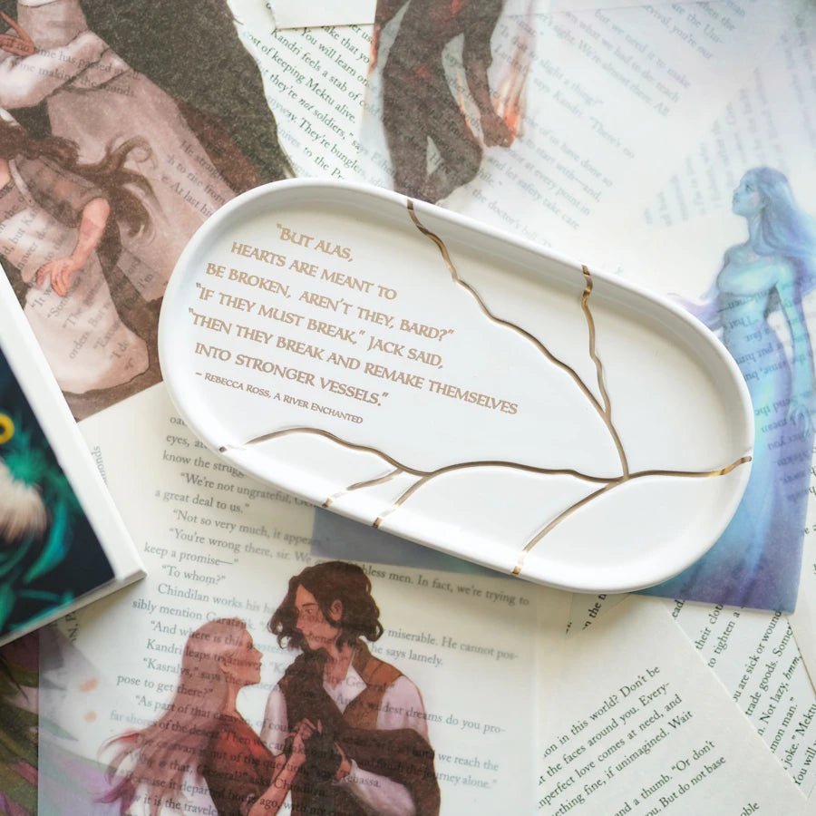 A River Enchanted Broken Heart Trinket Tray - a white ceramic tray with stylized golden cracks and a quote from Rebecca Ross