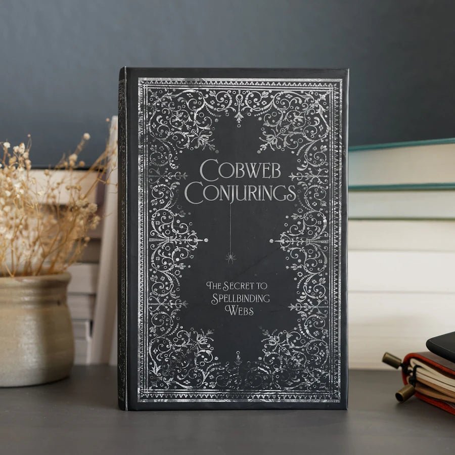 Black fake book with title "Cobweb Conjurings" and subtitle "The Secret to Spellbinding Webs" on gothic-style cover