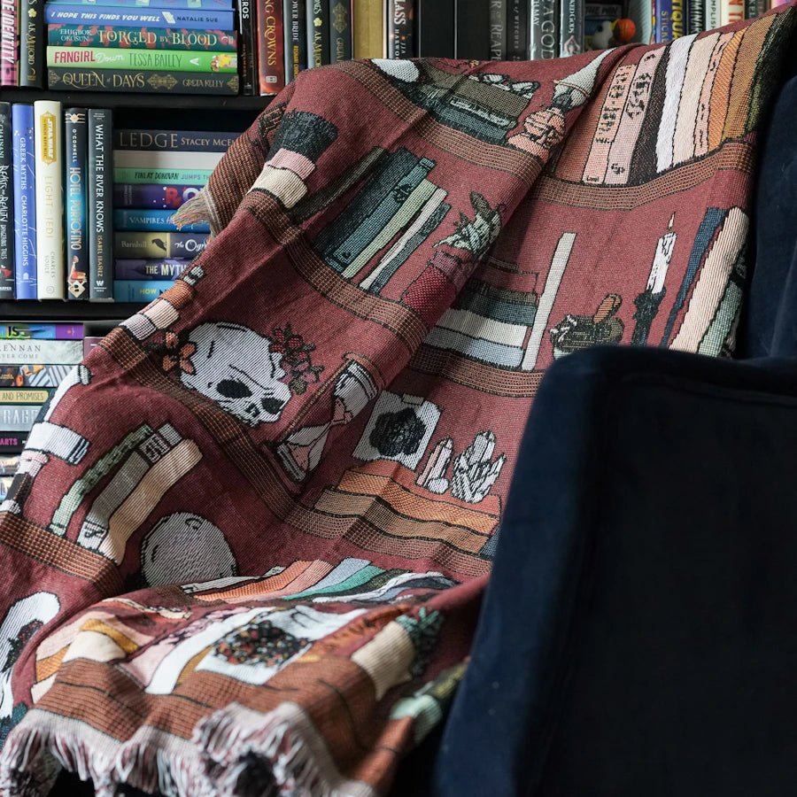 Dark Academia Bookshelf Woven Blanket—a jacquard woven blanket depicting a shelf including books, candles, potions, and more!