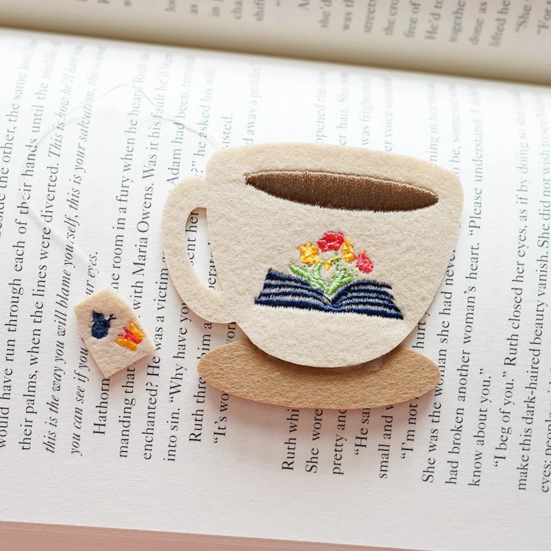 The Embroidered Tea Cup Bookmark features a whimsical teacup with an embroidered open book and delicate flowers.