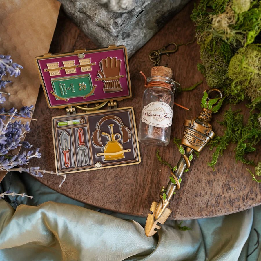 Herbology Key Collectible #19 shaped like a trowel with a root-shaped head, a suitcase charm, and a valerian root charm.