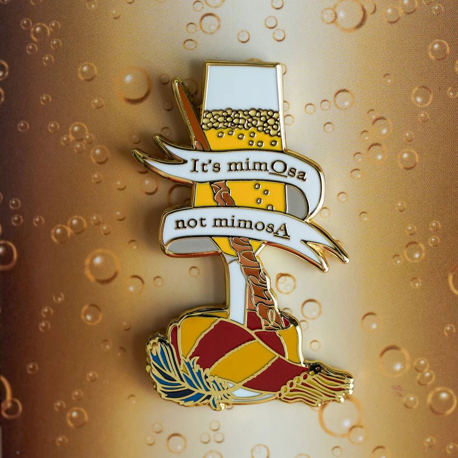 It&#39;s mimOsa not mimosA Cocktail Enamel Pin features a full champagne glass, a magic wand, and a gold and red scarf.