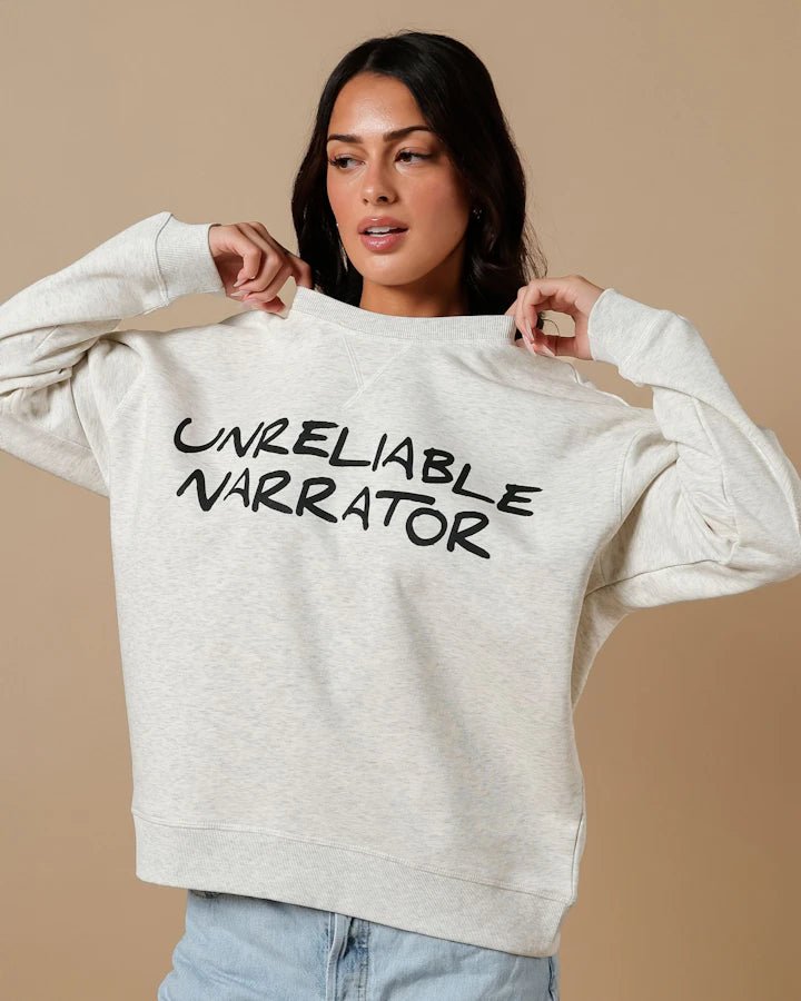 Unreliable Narrator Sweatshirt—pale heathered tan sweatshirt with crew neck that reads &quot;Unreliable Narrator&quot; across the chest