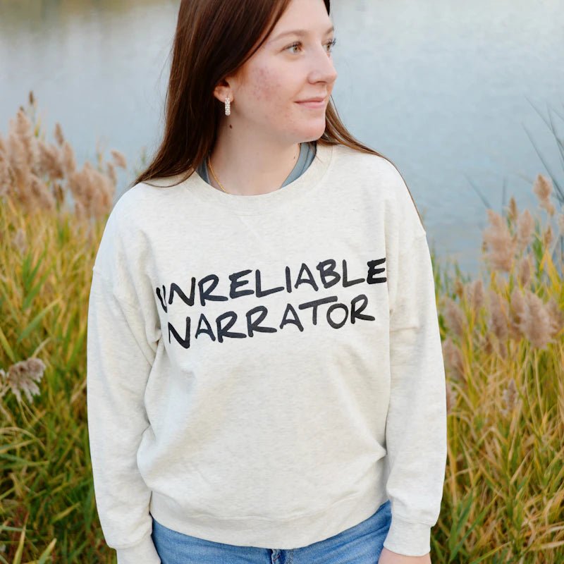 Unreliable Narrator Sweatshirt—pale heathered tan sweatshirt with crew neck that reads "Unreliable Narrator" across the chest