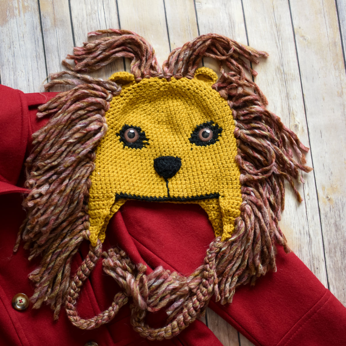 Lion hat with a knitted gold lion face and brownish red yarn mane.