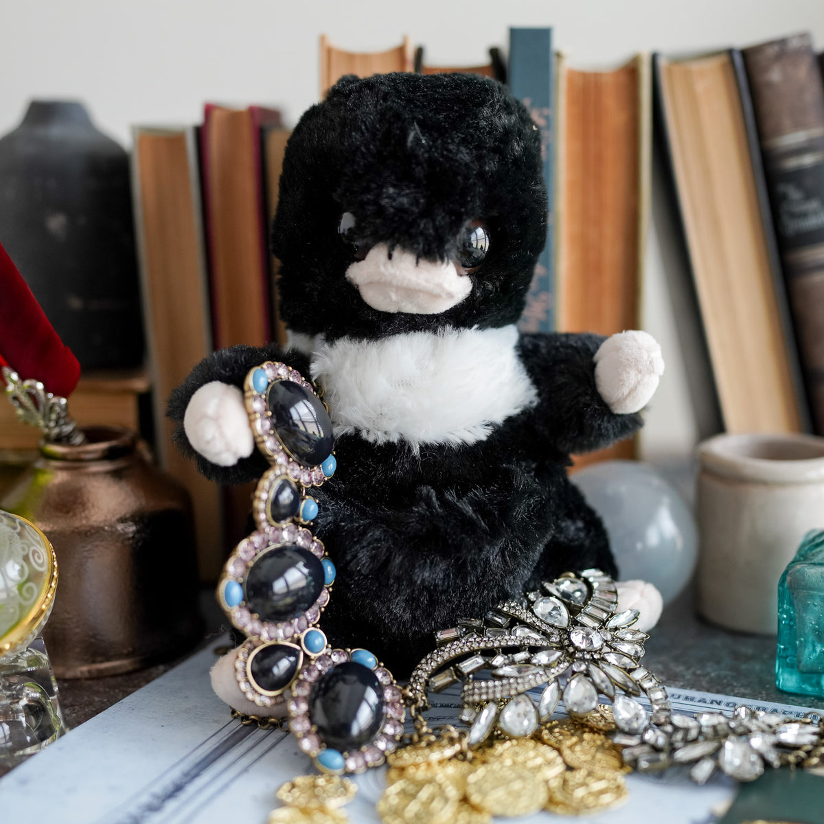 Thief Plush with jewels around it in front of a stack of books