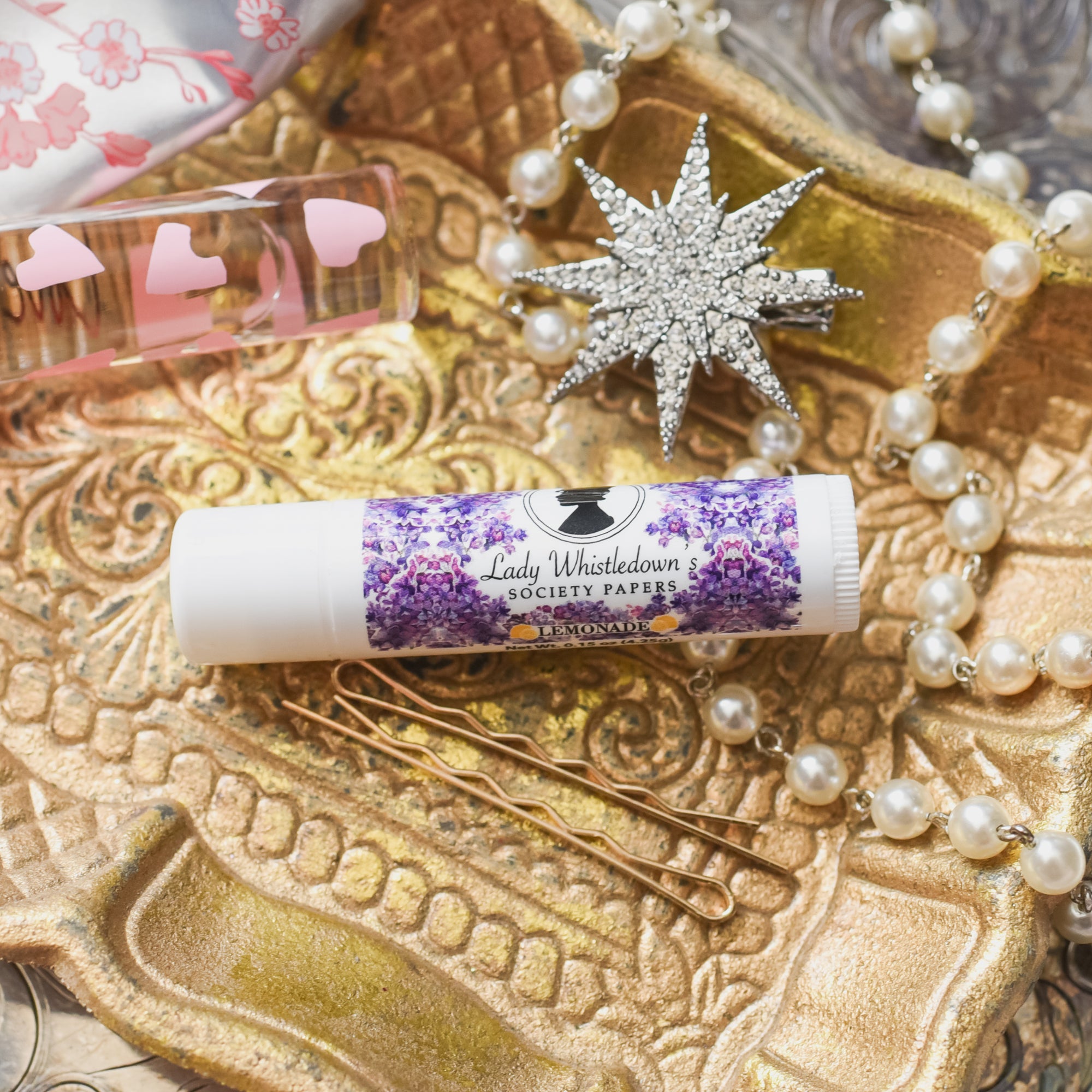 Bridgerton Lip Balm with a silhouette of a woman and printed with purple flowers and a lemonade flavor label on the side.