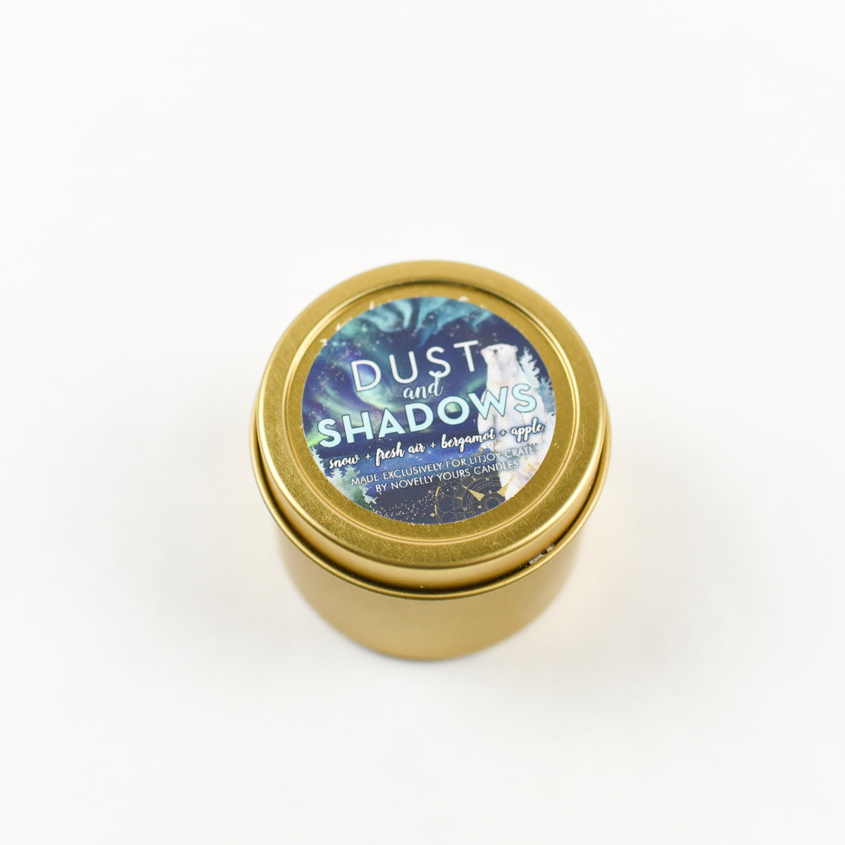 His Dark Materials Candle in a gold tin with the words &quot;Dust and Shadows&quot; on the lid