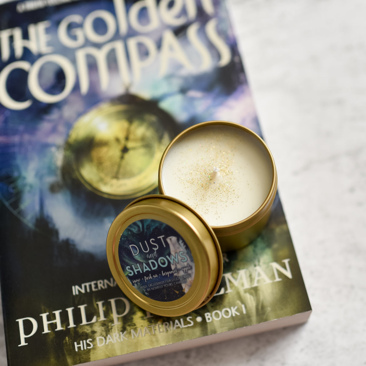 His Dark Materials Candle in a gold tin on top of The Golden Compass book by Philip Pullman
