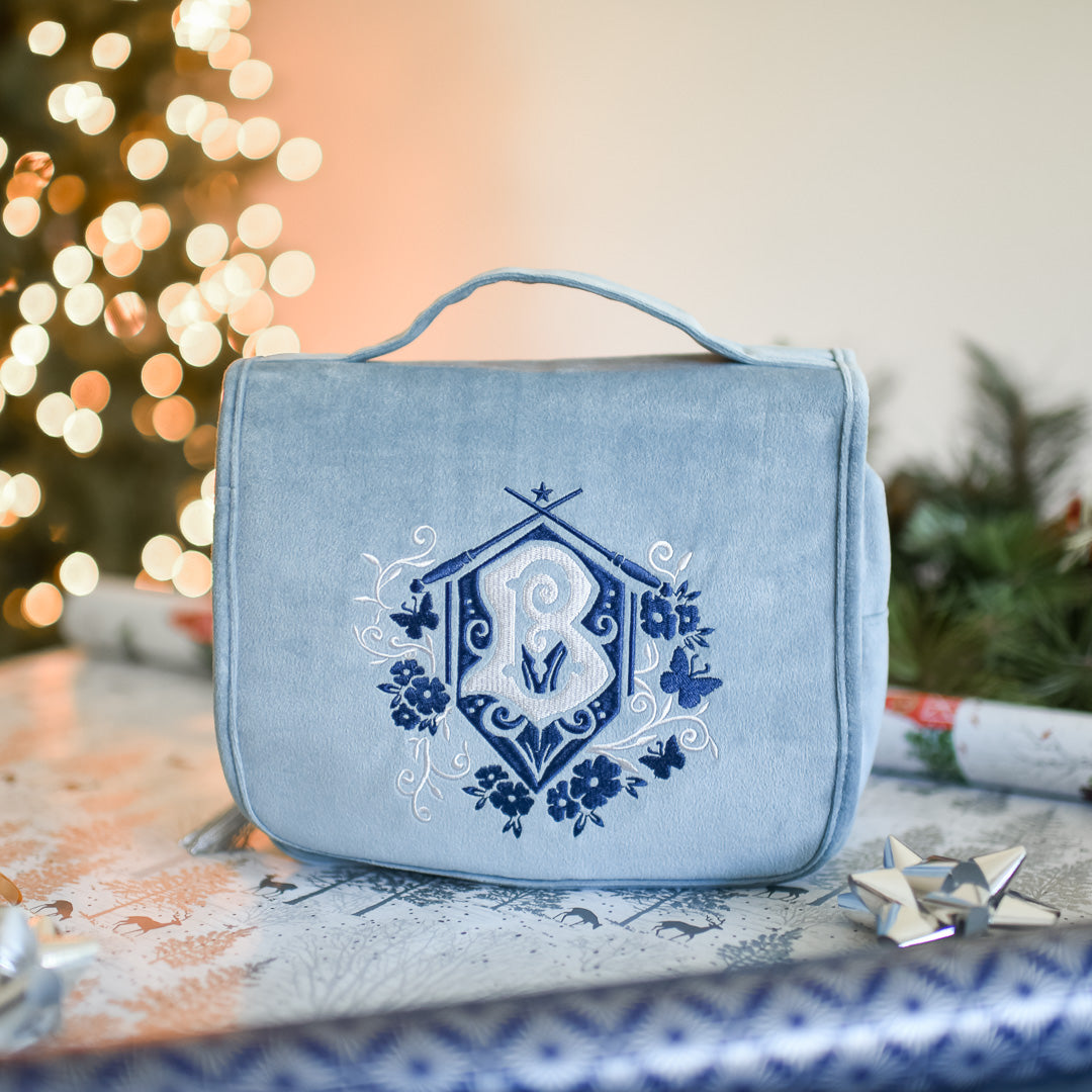 Baby blue French Academy of Magic Hanging Travel Bag has a flap with the embroidered school crest and a handle for carrying.