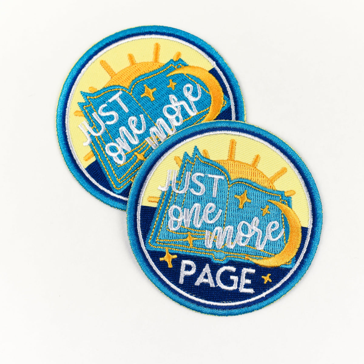 One More Page Patch is blue, yellow and white with a book, sun and moon and stars, and the words &quot;Just One More Page&quot;