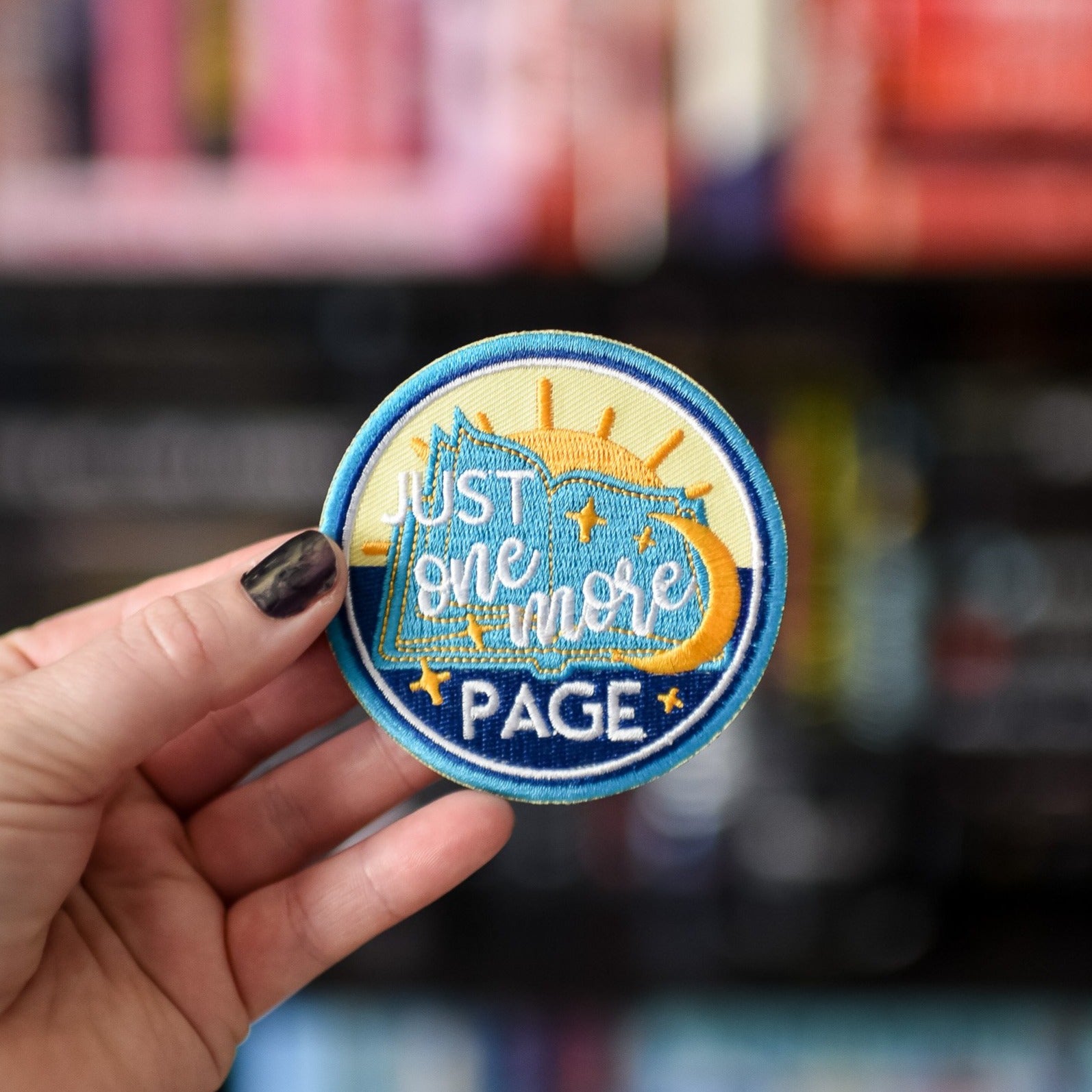 One More Page Patch is blue, yellow and white with a book, sun and moon and stars, and the words "Just One More Page"