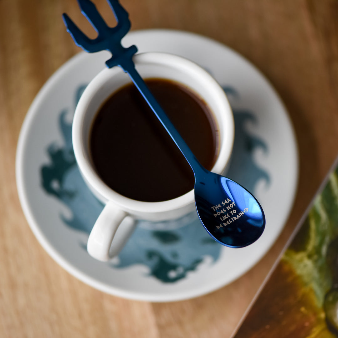 Metallic blue Demigod Teaspoon with a trident handle and the phrase "The sea does not like to be restrained"