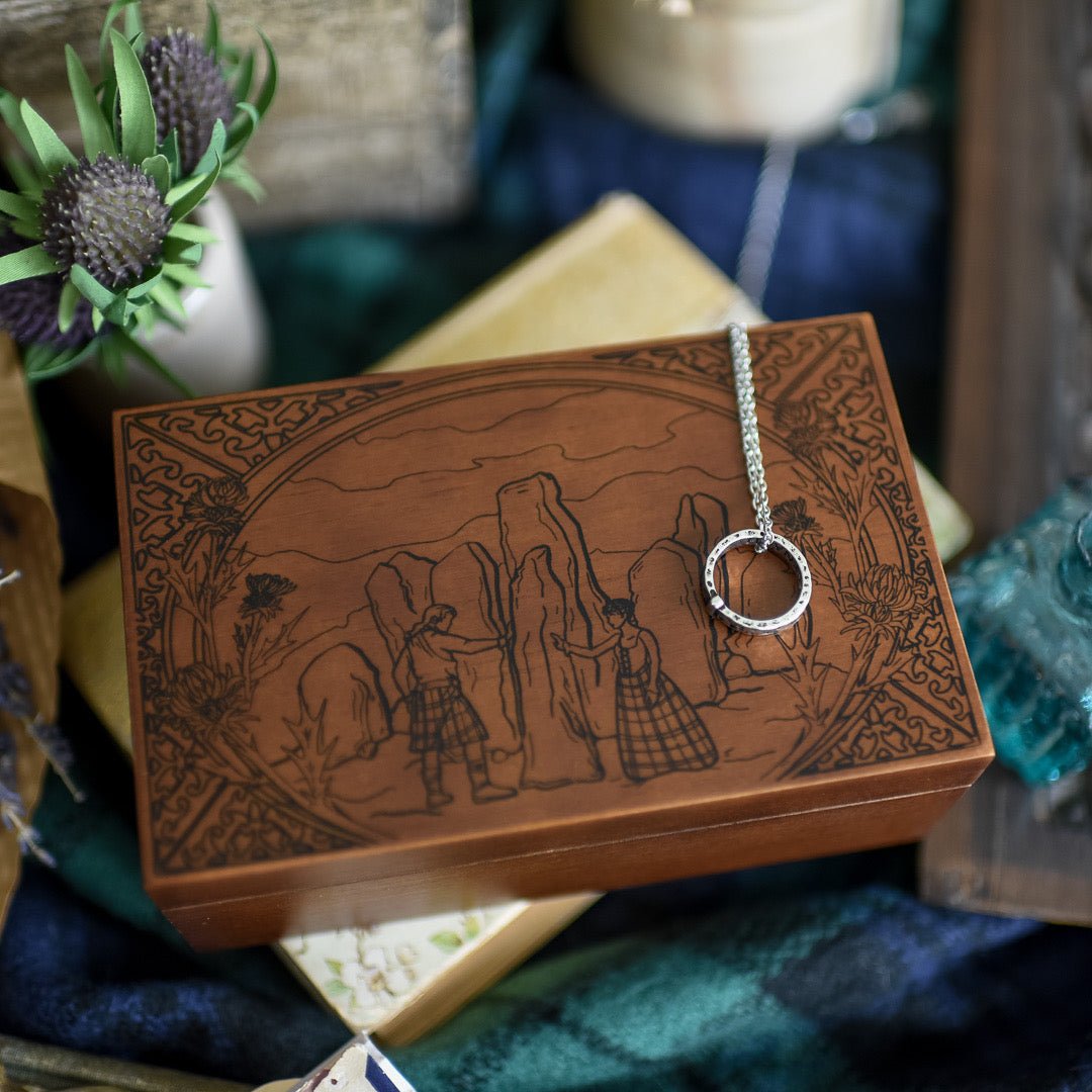Standing Stones Music Box is engraved with a man and woman with their hands on tall stones and dressed in Scottish clothes