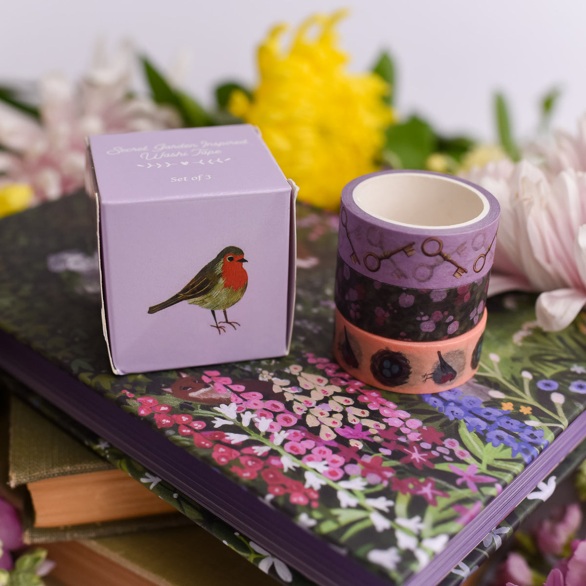 Secret Garden Set of 3 Washi Tape are 3 different patterns of tape stacked next to a purpple box with a robin bird on it