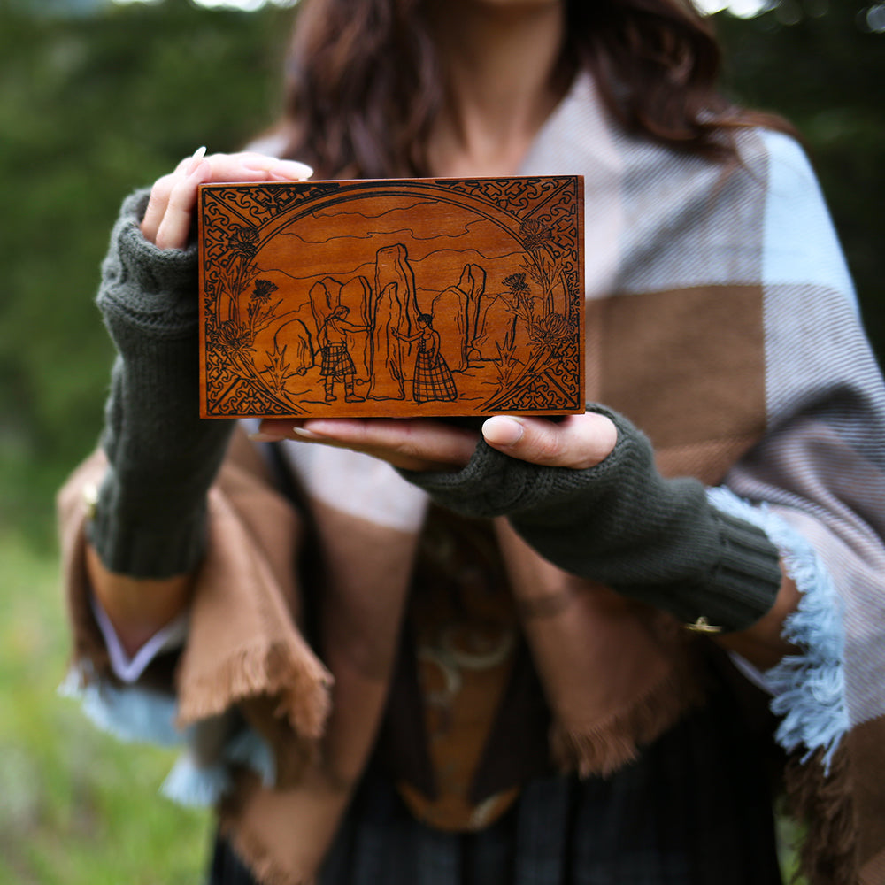 Standing Stones Music Box is engraved with a man and woman with their hands on tall stones and dressed in Scottish clothes