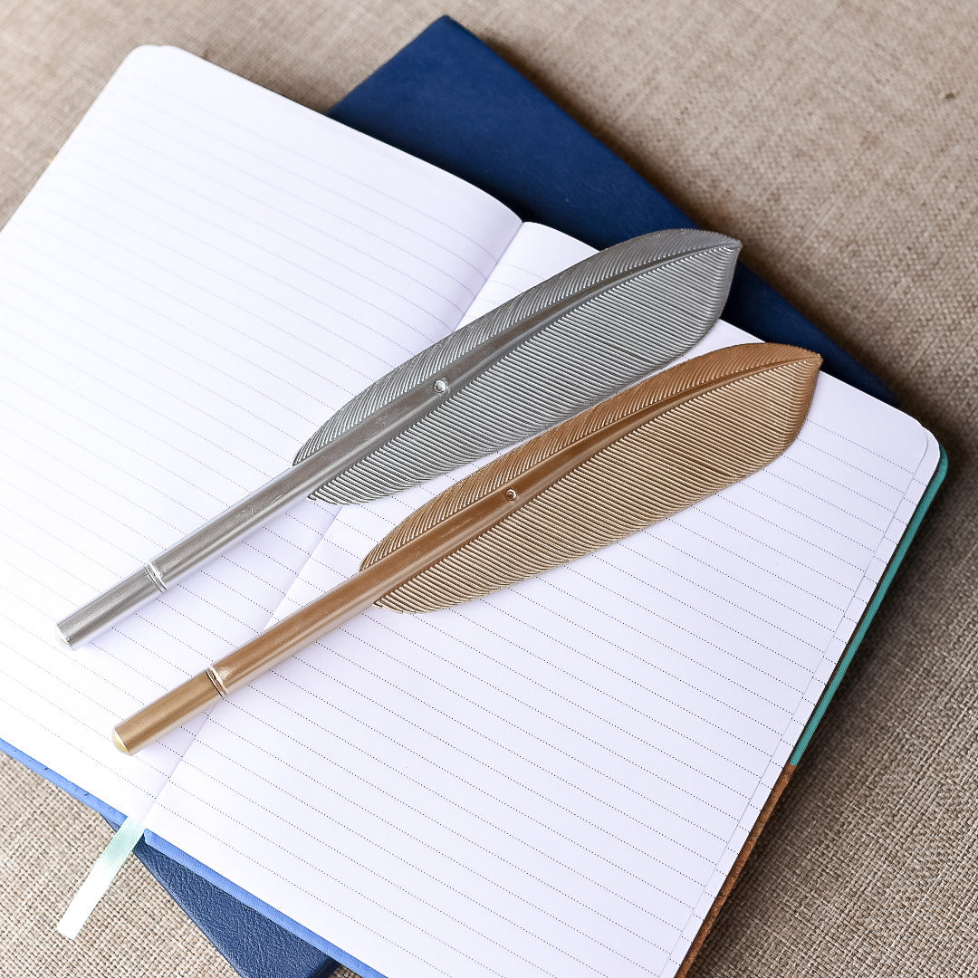 Gold and Silver Feather Pens with tip cover laying on a notebook 