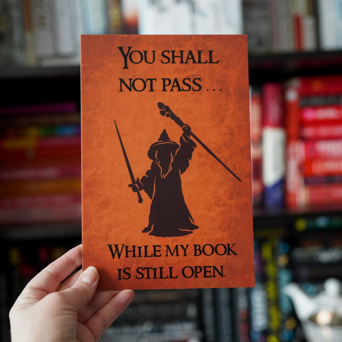 Gray Wizard Reading Sign has a brown leather background, a wizard holding a sword and staff, and the words &quot;You shall not pass . . . while my book is still open.&quot;