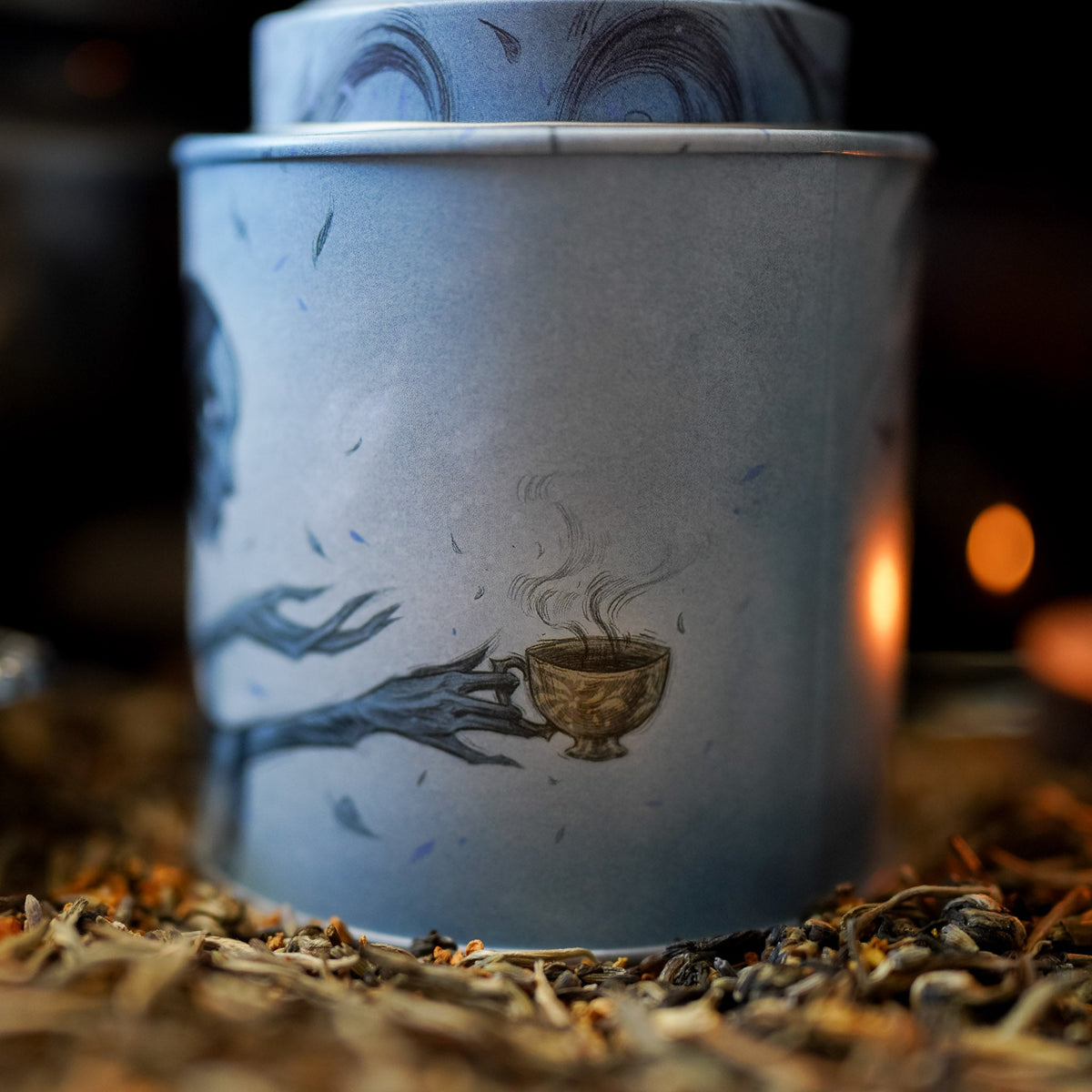 Suriel Tea Company Tin in blue and gray with a black Suriel from ACOTAR spilling the tea from a golden teacup.