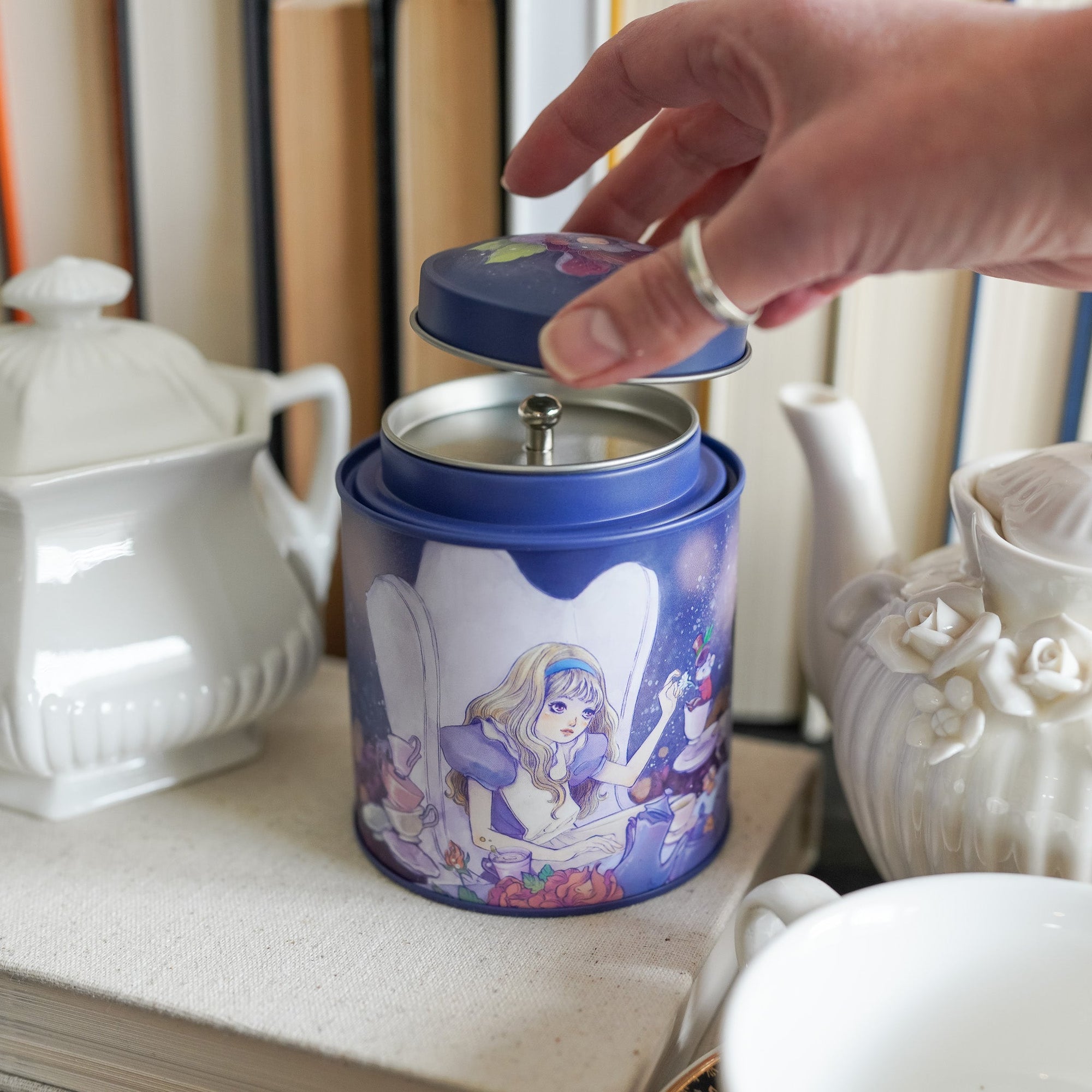 Round metal Alice in Wonderland Tea Tin with Alice, Mad Hatter, and Rabbit sitting at a table for tea time.