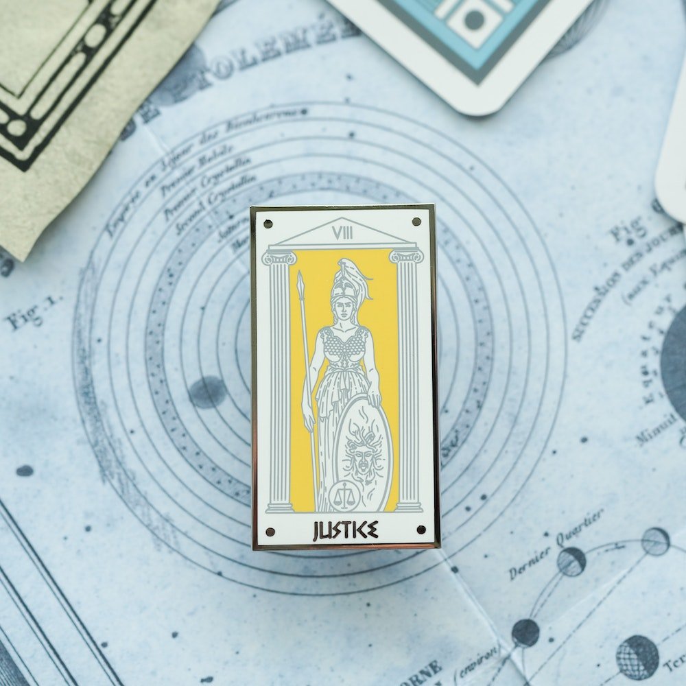 Athena Justice, Mythology Tarot Enamel Pin stands with the scales of justice at her feet and armored for war.