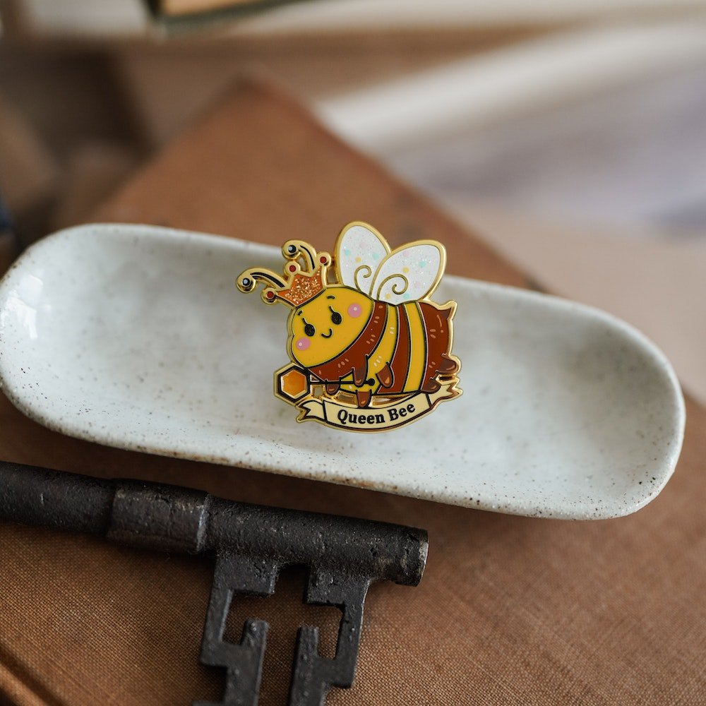 Book Bee Blind Bag Enamel Pin with images of a bee with text saying &quot;Queen Bee&quot;