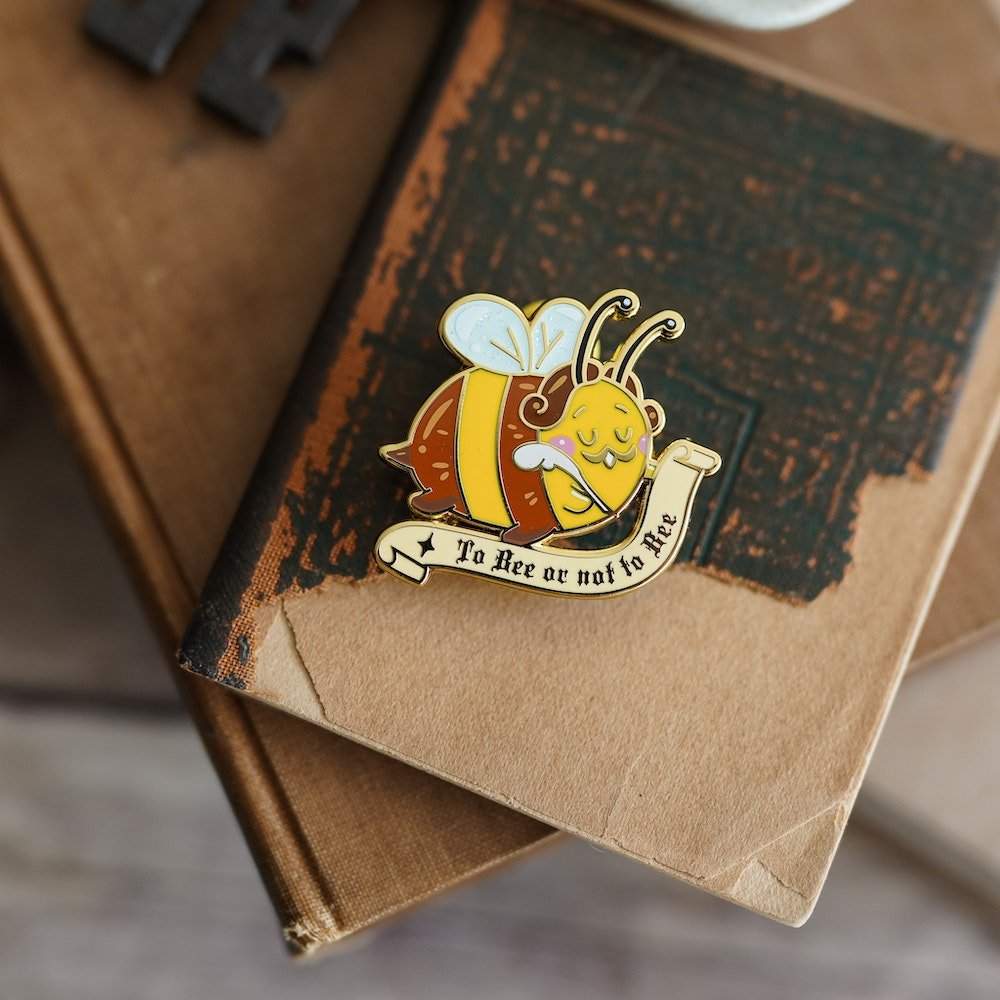 Book Bee Blind Bag Enamel Pin with images of a bee with text saying &quot;To Bee or Not To Bee&quot;