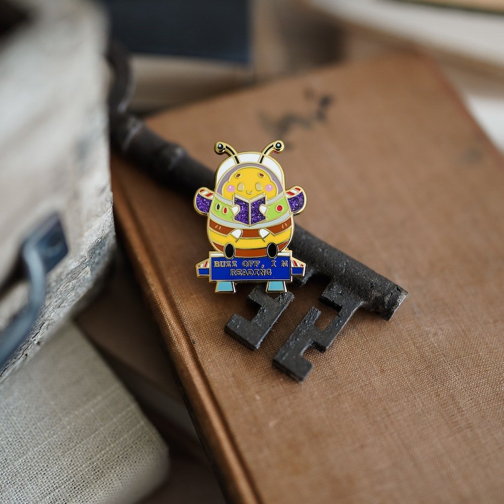 Book Bee Blind Bag Enamel Pin with images of a bee with text saying &quot;Buzz Off, I&#39;m Reading&quot;