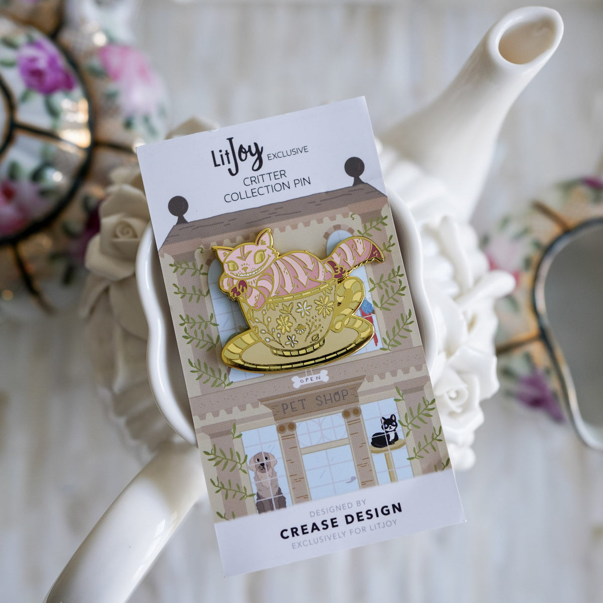 Chesire Cat Critter Collection Enamel Pin with a pink, striped, smiling cat sitting in a teacup on top of a saucer.