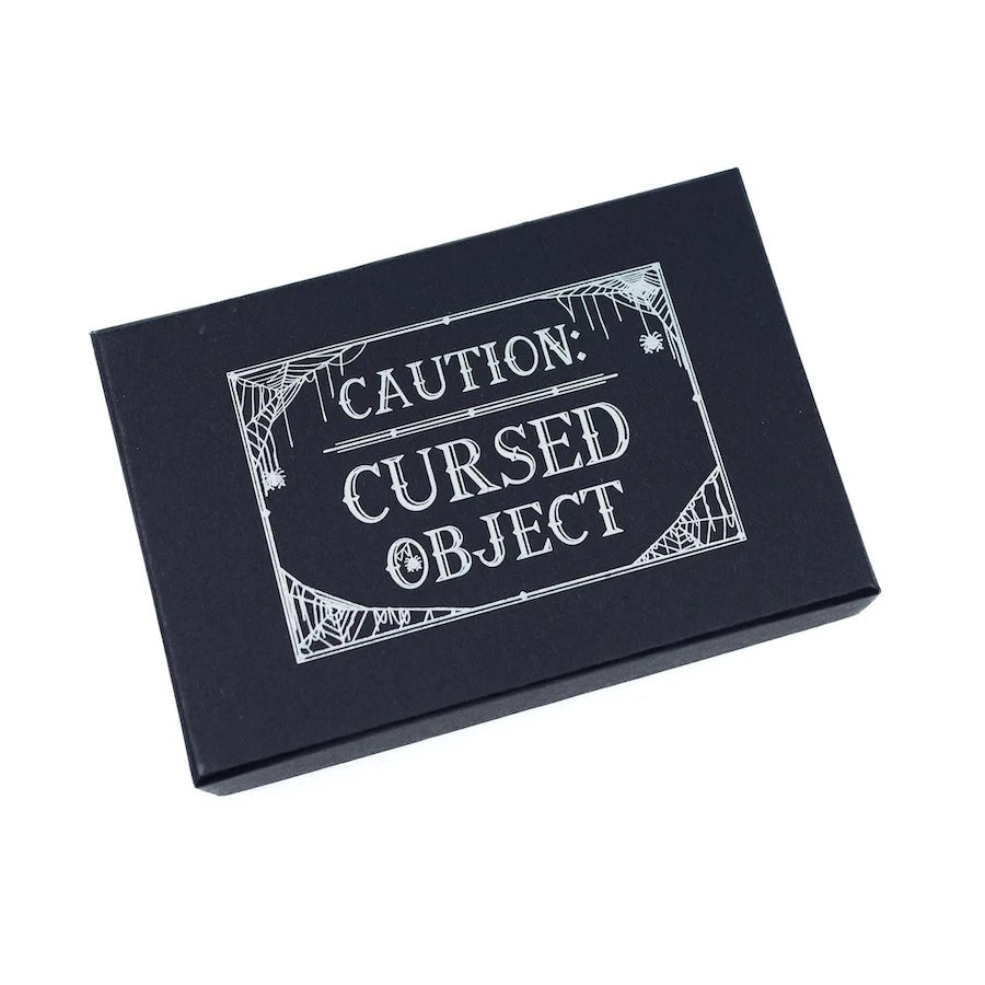 Cursed Opal Necklace Enamel Pin comes in a box with the words CAUTION: CURSED OBJECT
