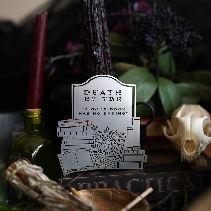 Death by TBR Metal Bookmark shaped like a tombstone with the words &quot;A good book has no ending&quot; and surrounded by flowers and books.