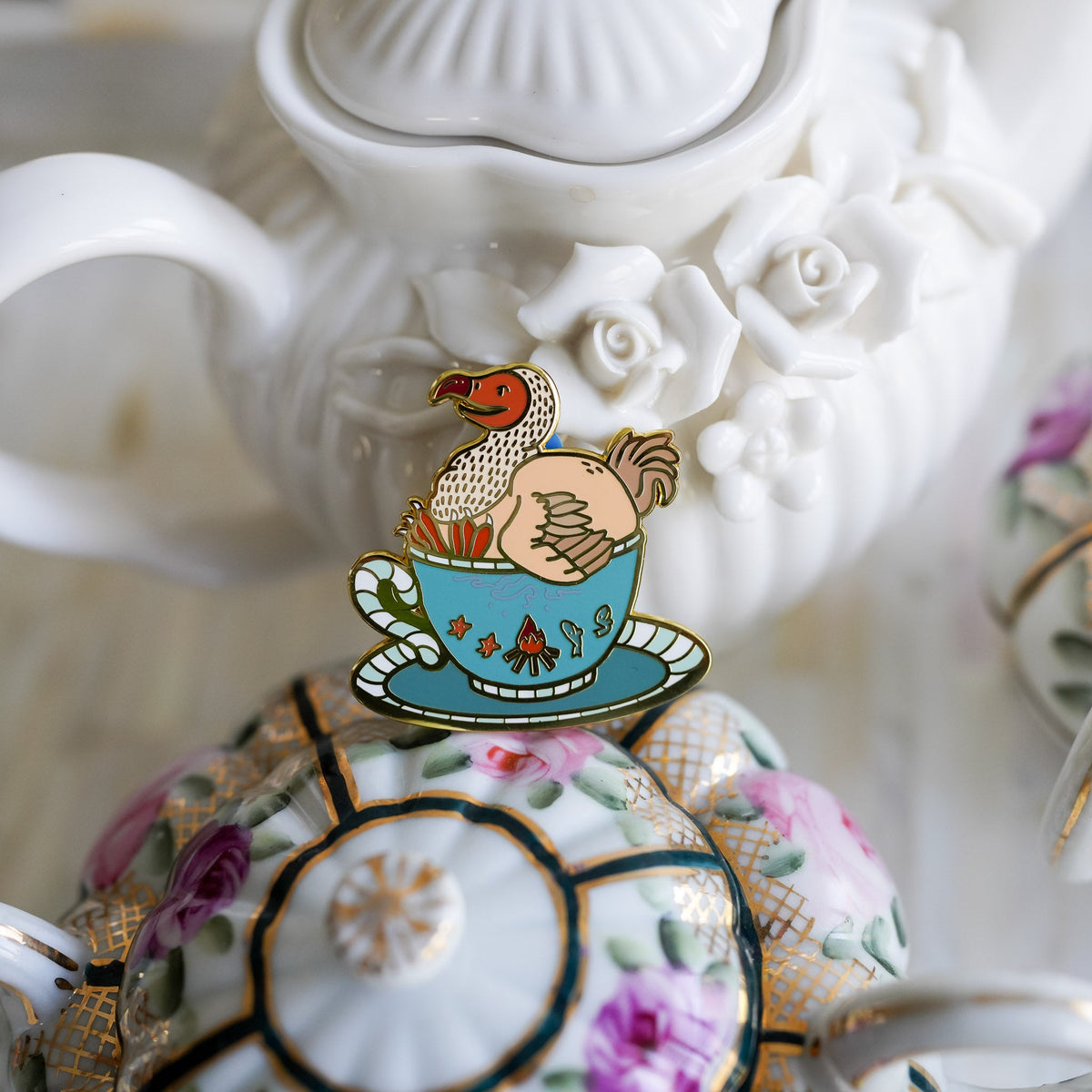 Dodo Bird Critter Collection Enamel Pin with a bird sitting inside of a teacup on top of a saucer.