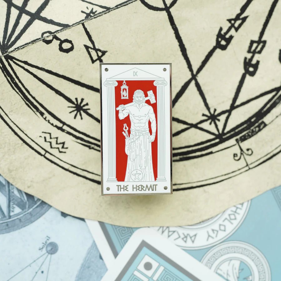 The Hephaestus The Hermit, Mythology Tarot Enamel Pin shows the god of fire with his tools standing before a red background.
