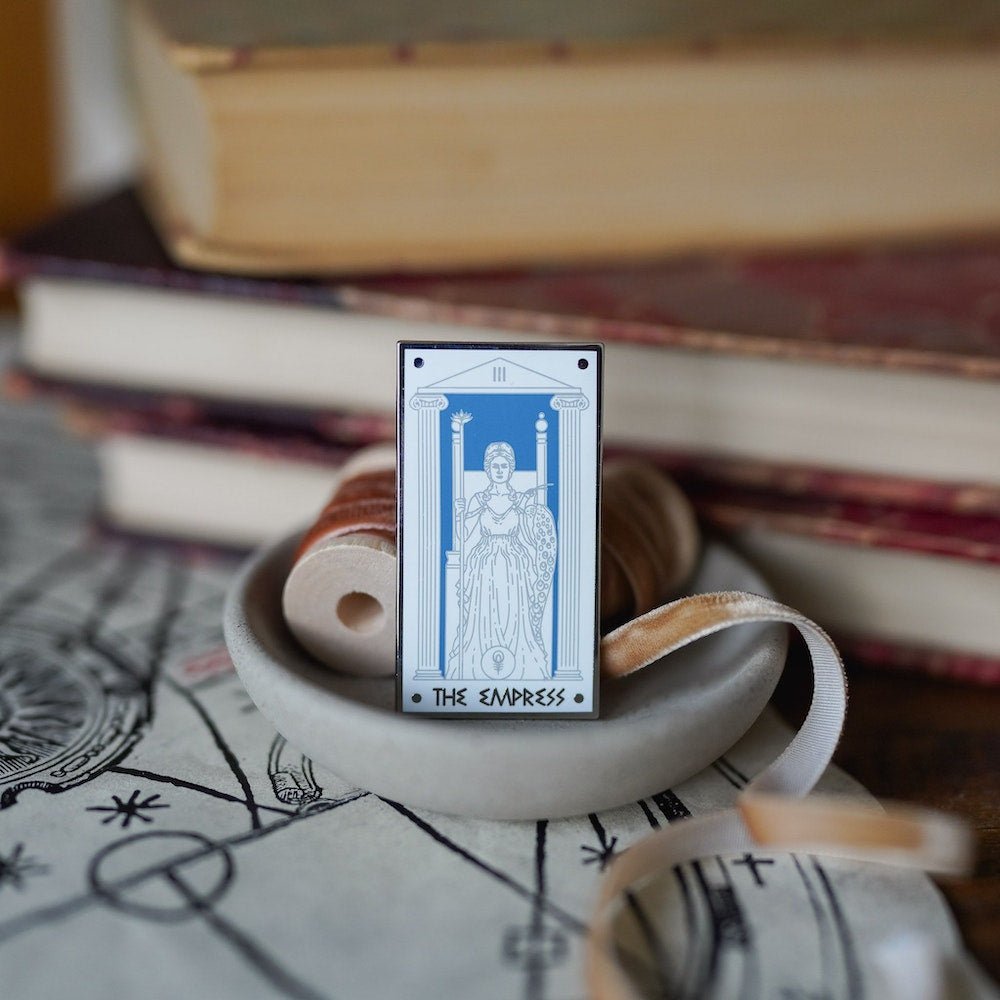 Hera The Empress, Mythology Tarot Enamel Pin with Hera sitting on a throne between two columns and words &quot;The Empress” below.
