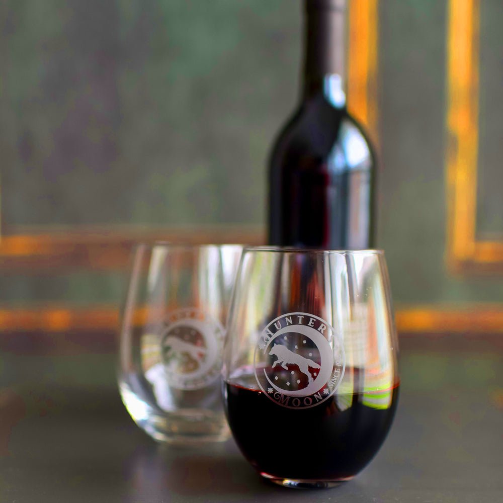 Hunter&#39;s Moon Stemless Wine Glass has an etched Hunter&#39;s Moon logo on a clear glass which includes a moon and wolf design