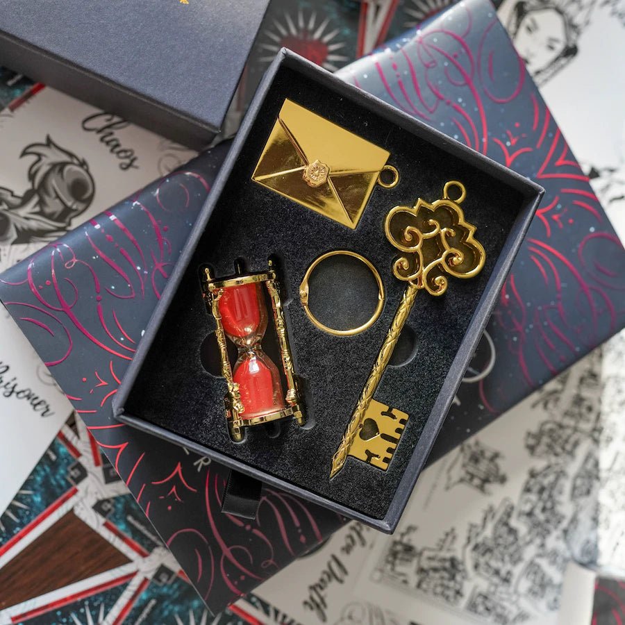 A key including two charms: an hourglass game piece with red sand, and an envelope with the engraved ticket inside