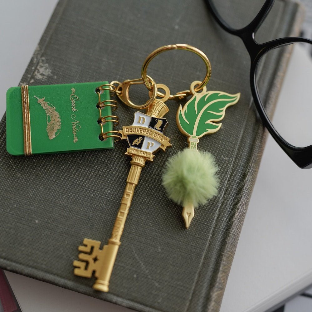 Gold Magical Newspaper Key with a wizard newspaper on the head, a quill with pompom, and an acid green small notebook charm