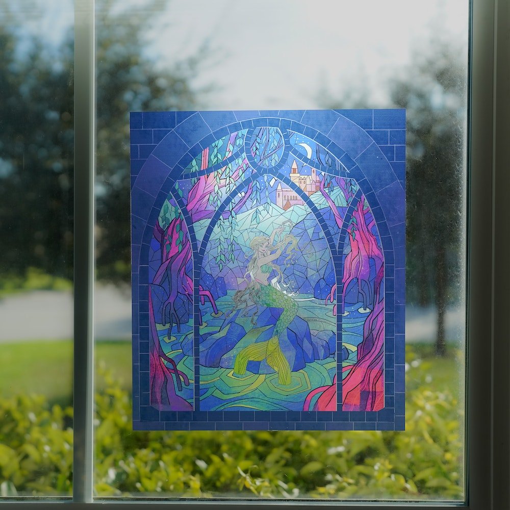 Mermaid Stained Glass Window Cling with an image of a mermaid on a lake surrounded by trees and a castle.