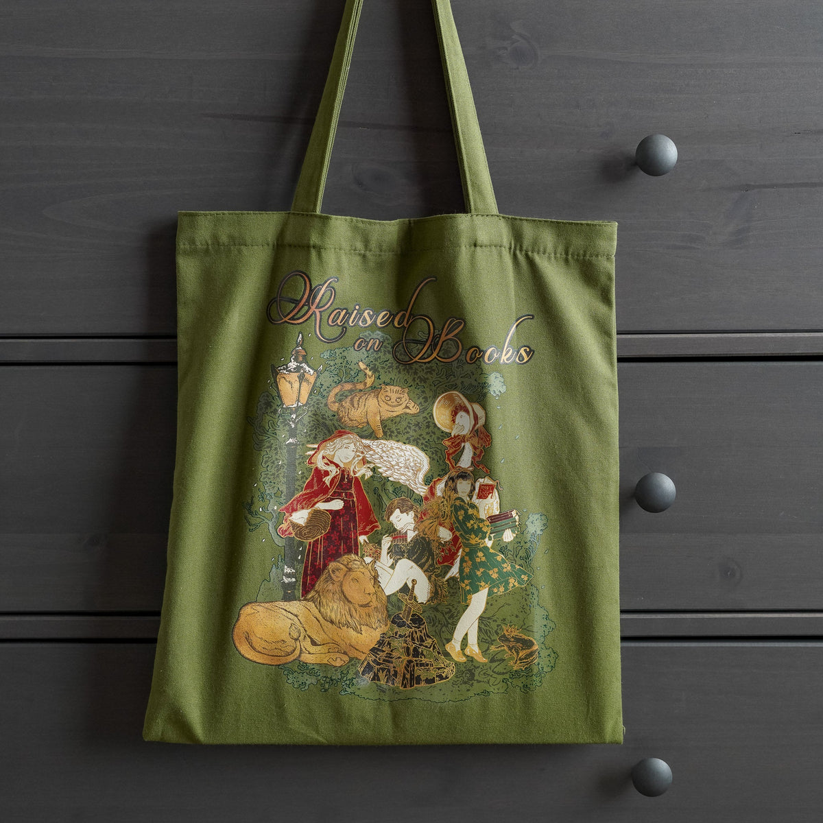 Raised on Books Tote featuring storybook characters in green, gold, and red colors.