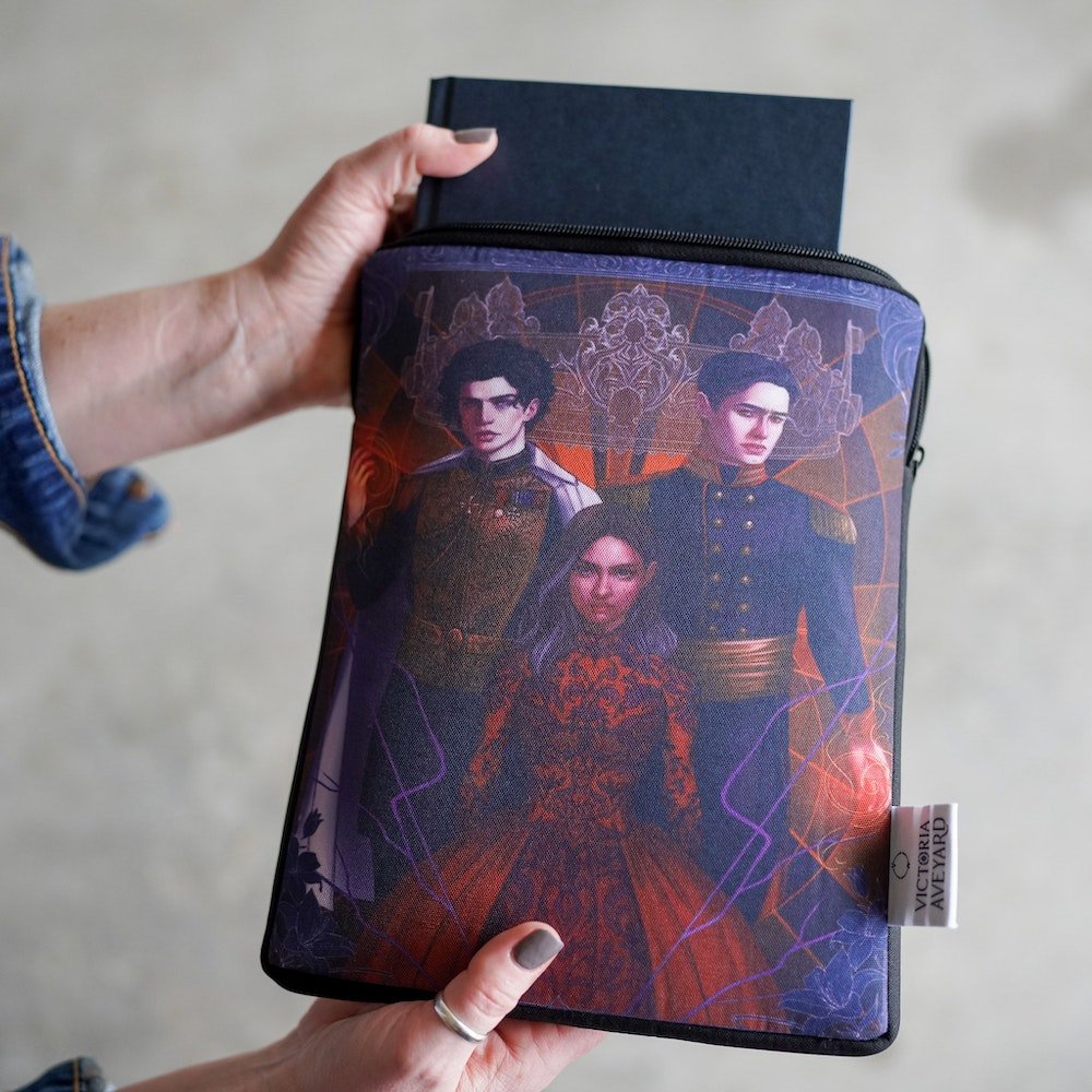 Red Queen Book Sleeve with fan art of Cal, Maven, and Mare with a crown behind them and a dark floral frame around them.