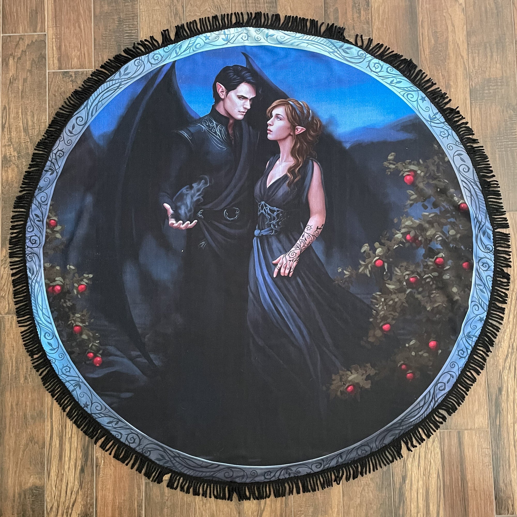 Round towel with fringe edge. Rhysand & Feyre in black. Rhysand has magic misting from his hand. Bushes of red fruit frame them.