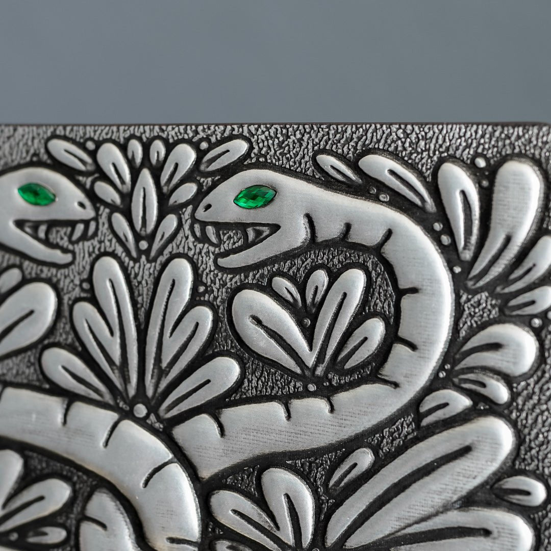 A closeup of the Snake Chamber Notebook with a faux metal cover with two intertwined snakes with green gem eyes